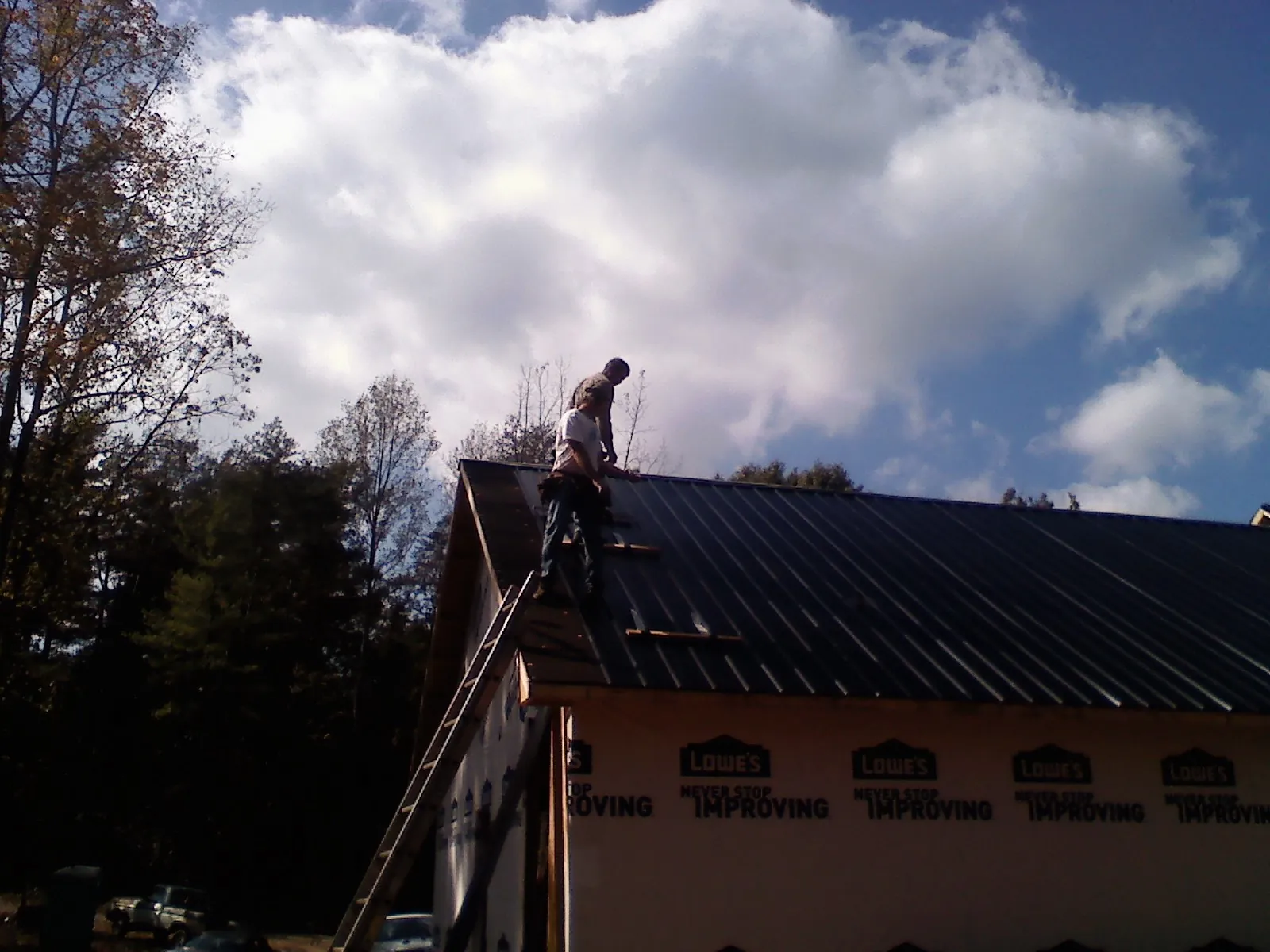 Roofer fastening dark metal panels high against a cloudy sky, from a Roof Inspection job in Monroe
